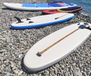 4 paddle boards laying out on a stone beach by the water